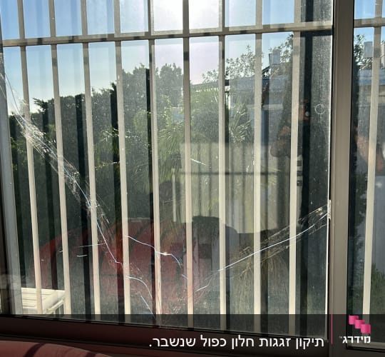 חלון זכוכית עם סדקים ותריסים ברקע